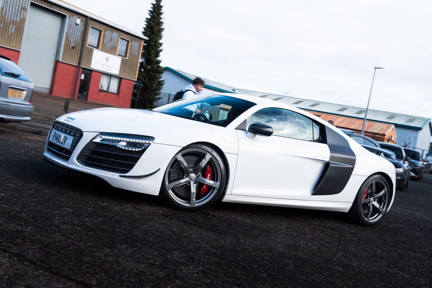 White Audi R8 supercar parked in an industrial area on a cloudy day.