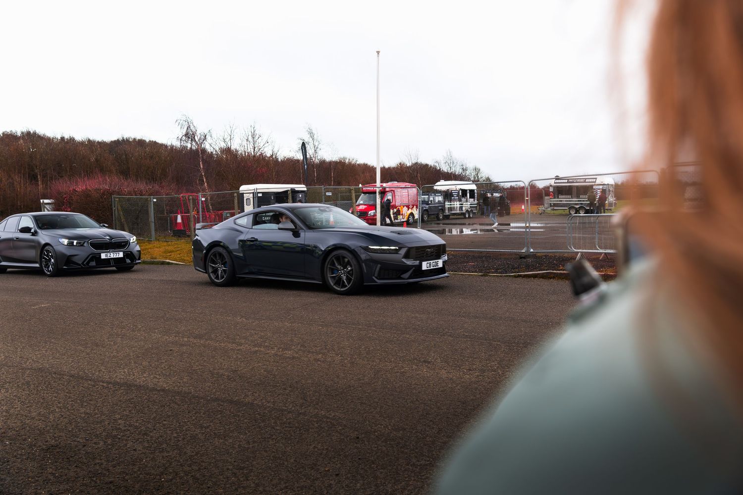 Gray Ford Mustang driving at a UK car meet event on an overcast day.