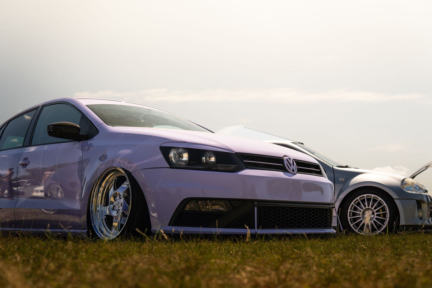Lowered purple Volkswagen Polo on wide stance wheels parked on grass at a car meet.
