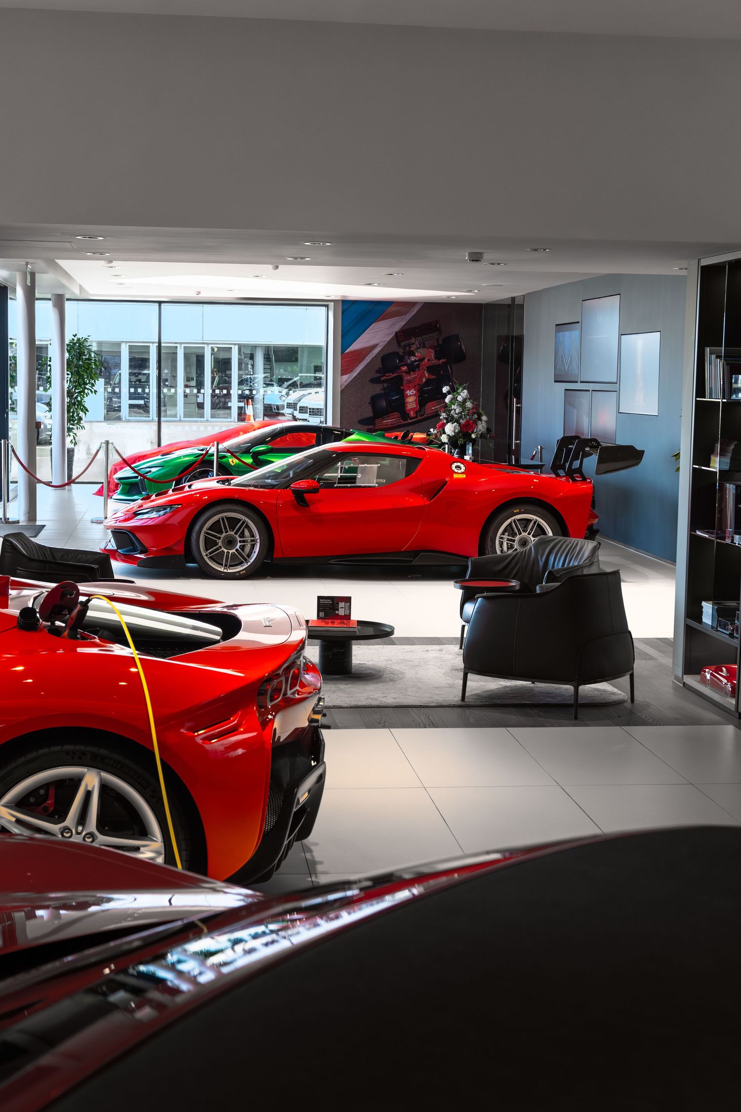 Luxury Ferrari showroom displaying multiple red sports cars including a racing model with colorful livery on a polished tile floor.