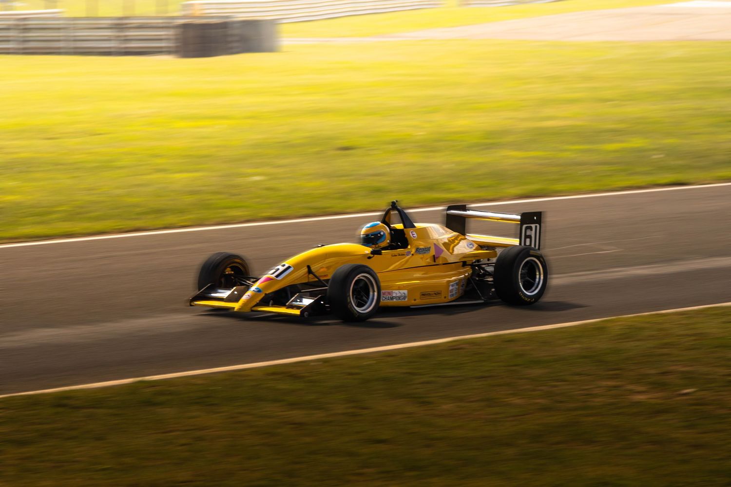Yellow Formula racing car speeds along a sunlit race circuit during a motorsport event.
