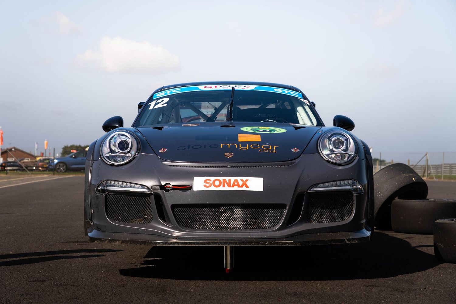 Front view of a grey Porsche 911 GT3 race car with SONAX sponsorship on a racing circuit.