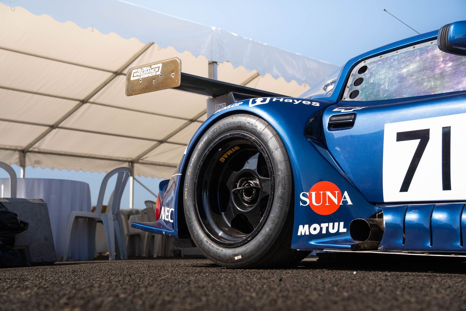 Blue Porsche GT racing car number 71 with Motul and Suna sponsorship in paddock.
