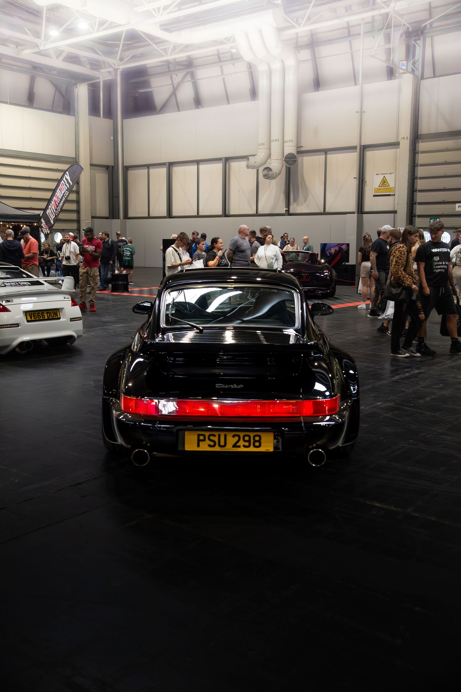 Rear view of a black Porsche 993 911 with registration PSU298 at an indoor car show.