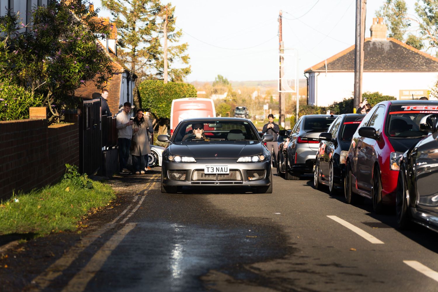 Modified Nissan Silvia S14 driving through a narrow residential street lined with spectators.