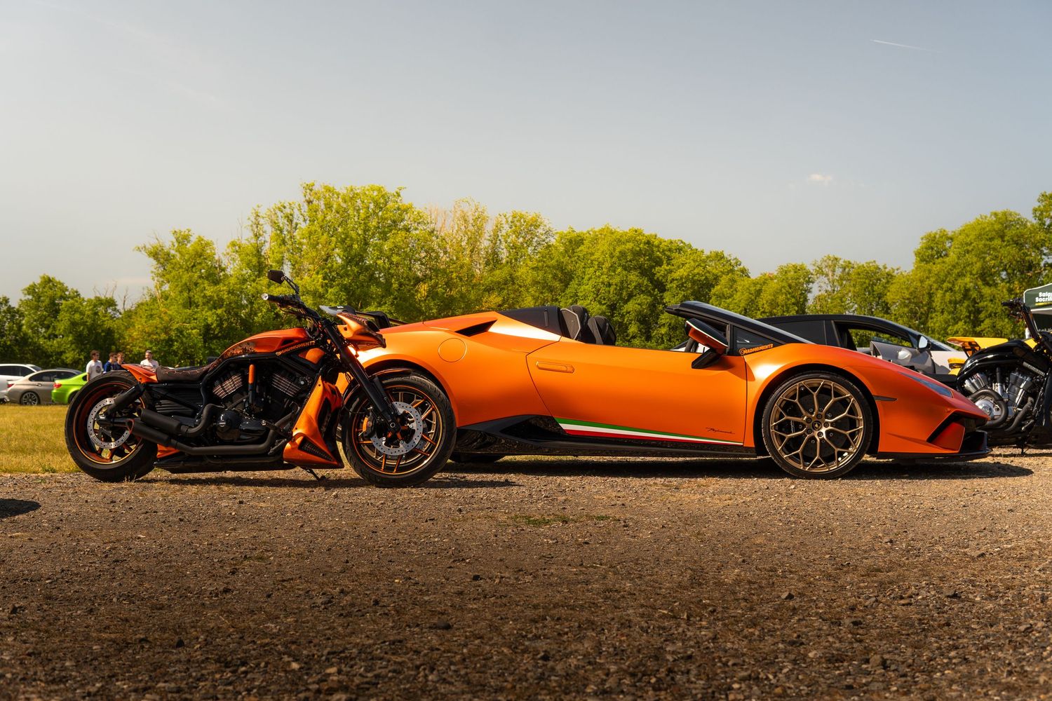 Orange Lamborghini Huracan Spyder parked beside a matching orange motorcycle at a car show.