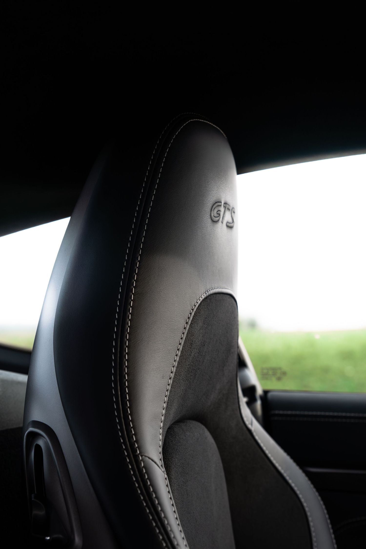 Close-up of a black leather Porsche GTS sport seat headrest with embroidered GTS logo inside a sports car.
