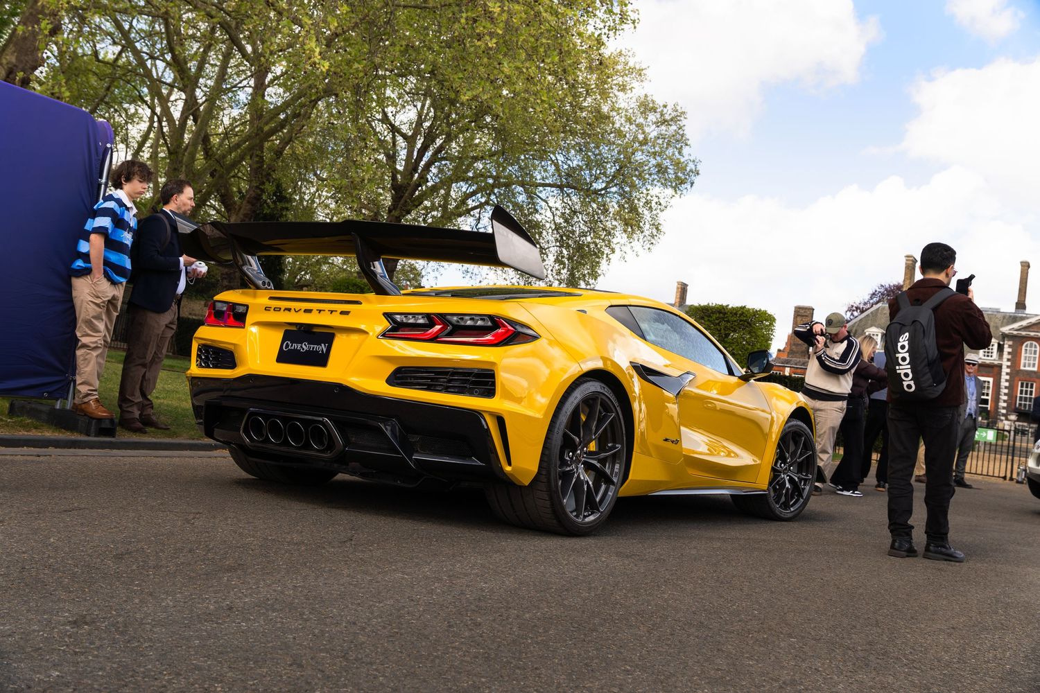 Rear view of a yellow Corvette Z06 sports car at an outdoor automotive event with spectators.