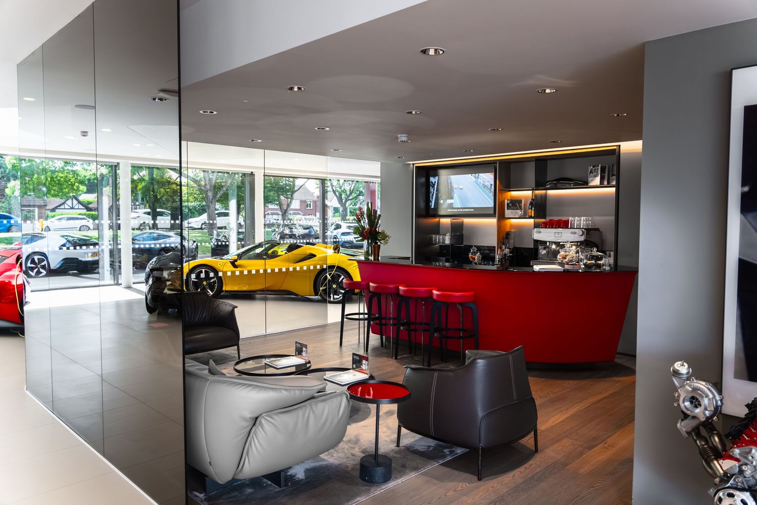 Luxury Ferrari dealership showroom with yellow sports car, red reception desk, and modern gray seating area.