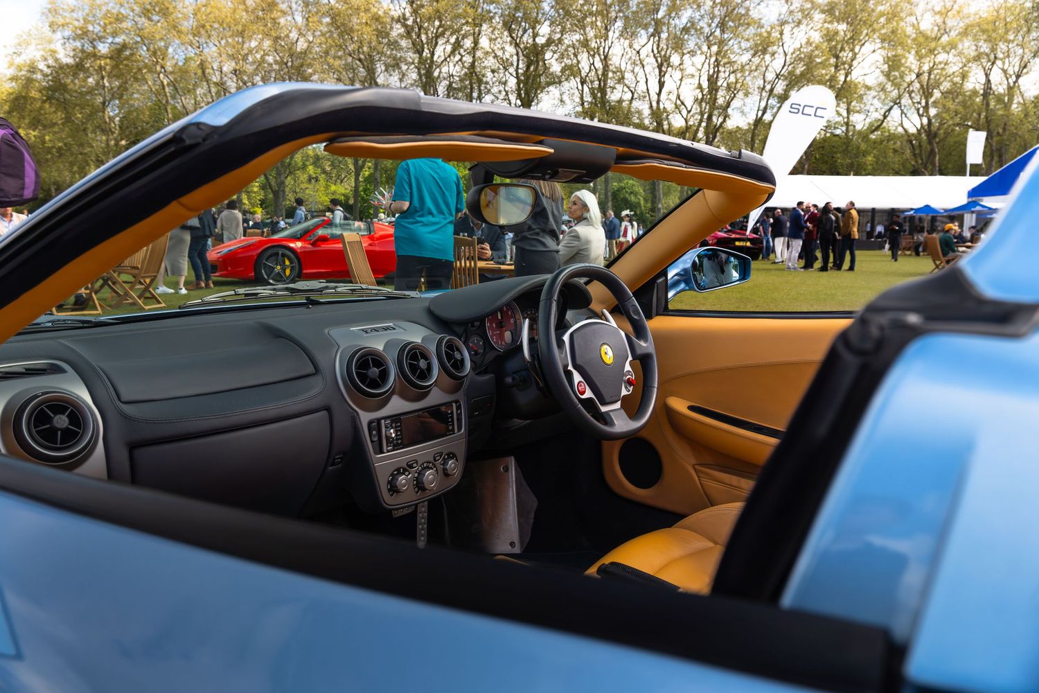 Interior view of a blue Ferrari F430 Spider convertible showing tan leather seats and dashboard.