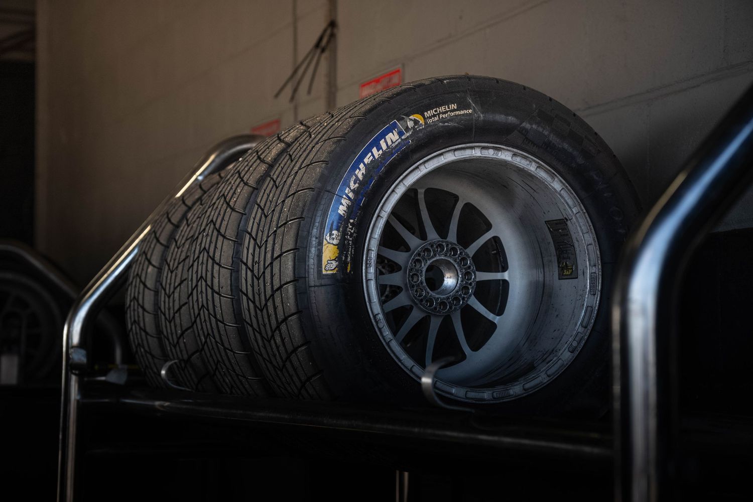 Pirelli racing slick and wet weather tyres stacked on a rack in a motorsport garage.