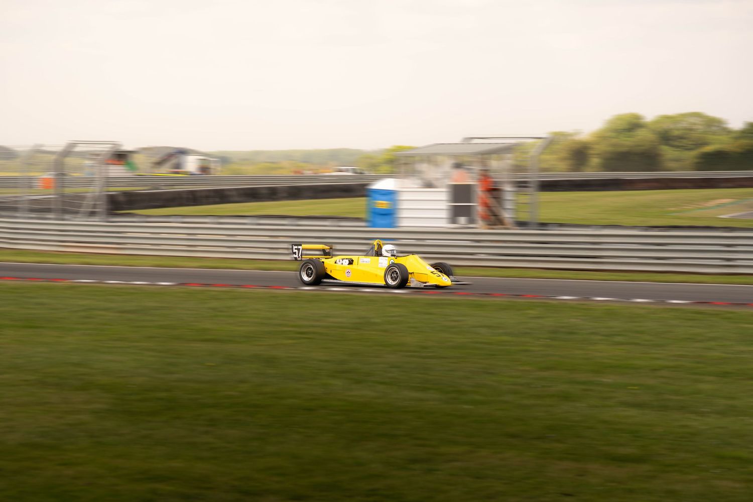 Yellow open-wheel sports racing car speeding along a race circuit.