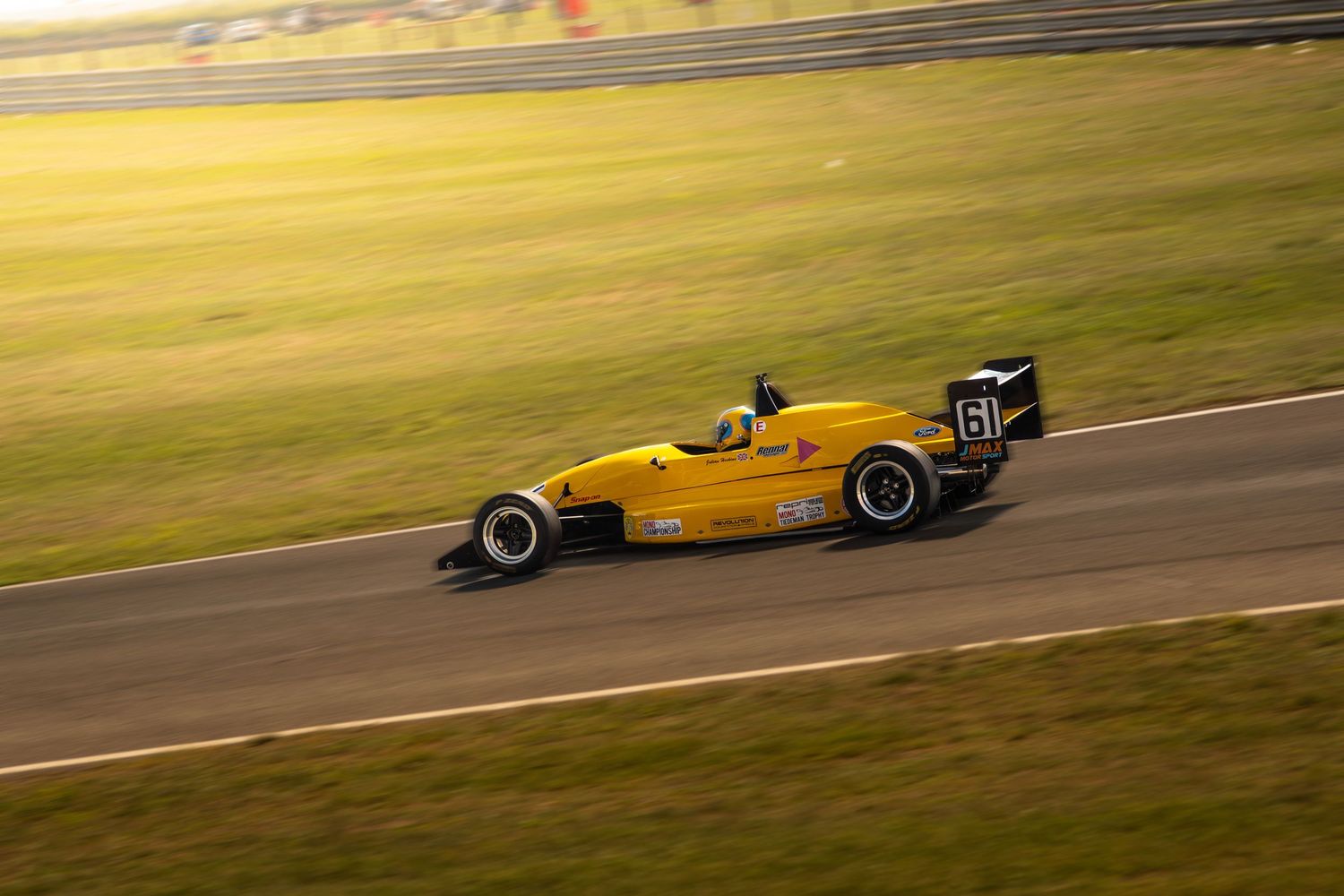 Yellow Formula racing car number 61 speeding along race track in golden sunlight.