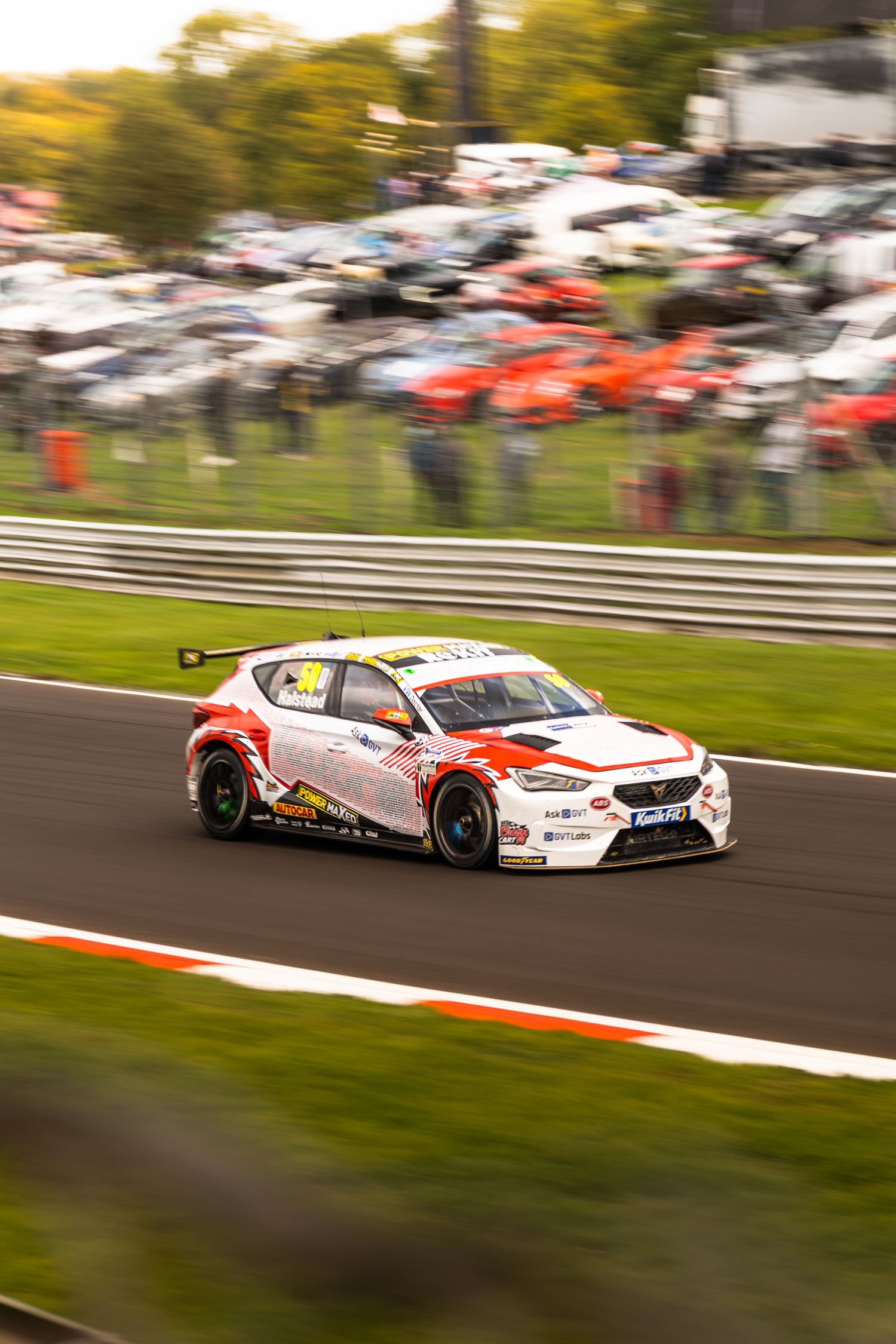 Red and white BTCC Ford Focus race car speeding around Brands Hatch circuit with motion blur.