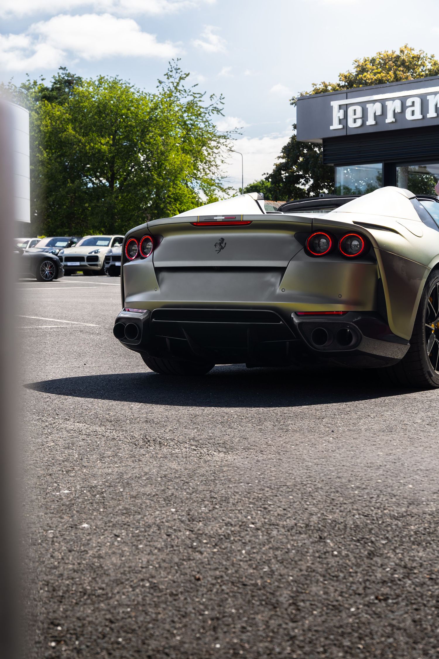 Rear view of a silver Ferrari supercar parked outside a Ferrari dealership on a sunny day.