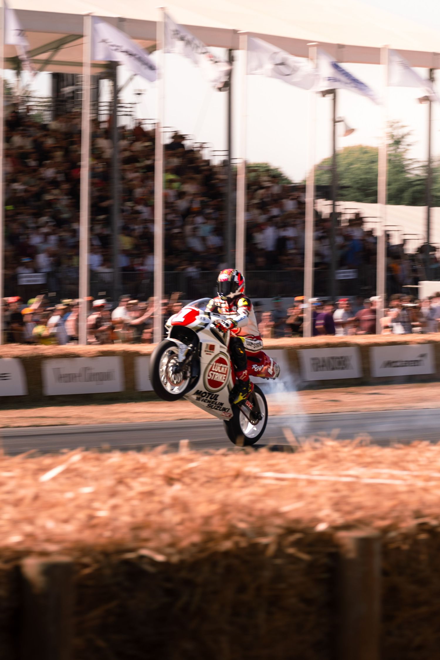 Motorcyclist performing a wheelie stunt at Goodwood Festival of Speed with crowd watching.