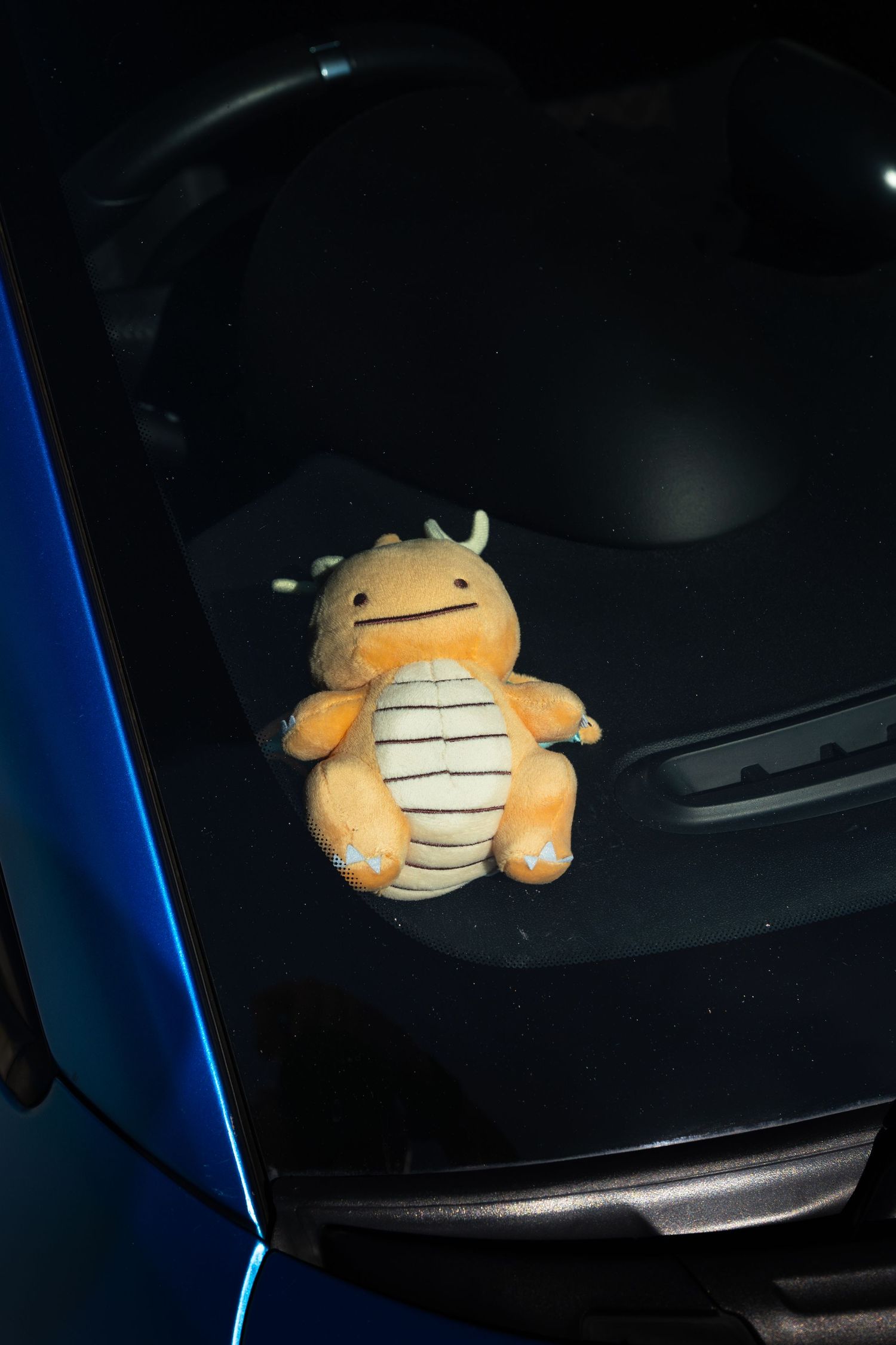 Dragonite Pokemon plush toy sitting on the parcel shelf of a blue car.
