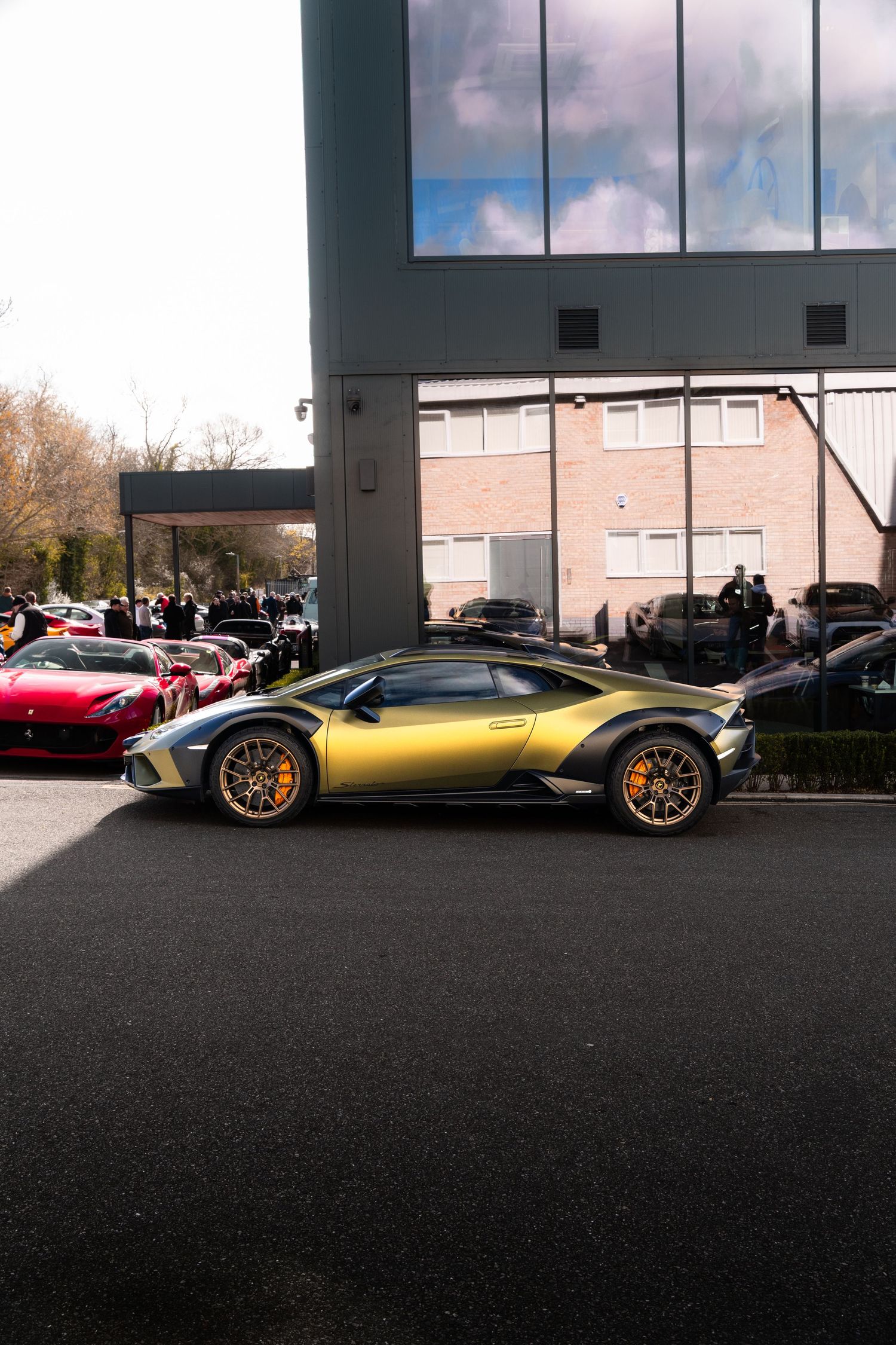 Gold and green Lamborghini Huracan Sterrato parked outside a modern building on a sunny day.