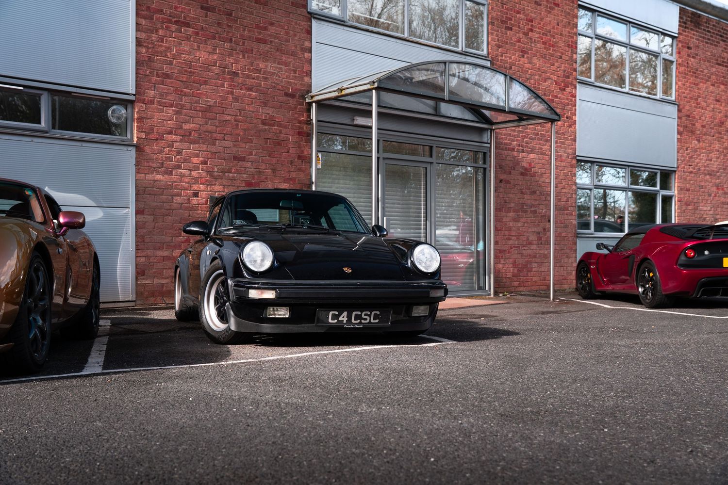 Black Porsche 930 Turbo with C4CSC plate outside brick dealership building.