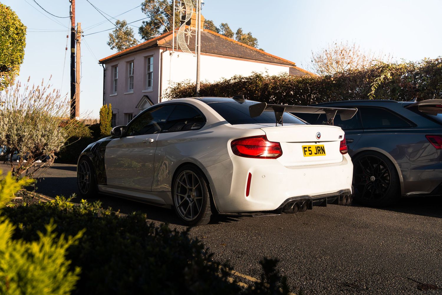White BMW M2 with large rear spoiler and dark alloy wheels parked at a car meet.