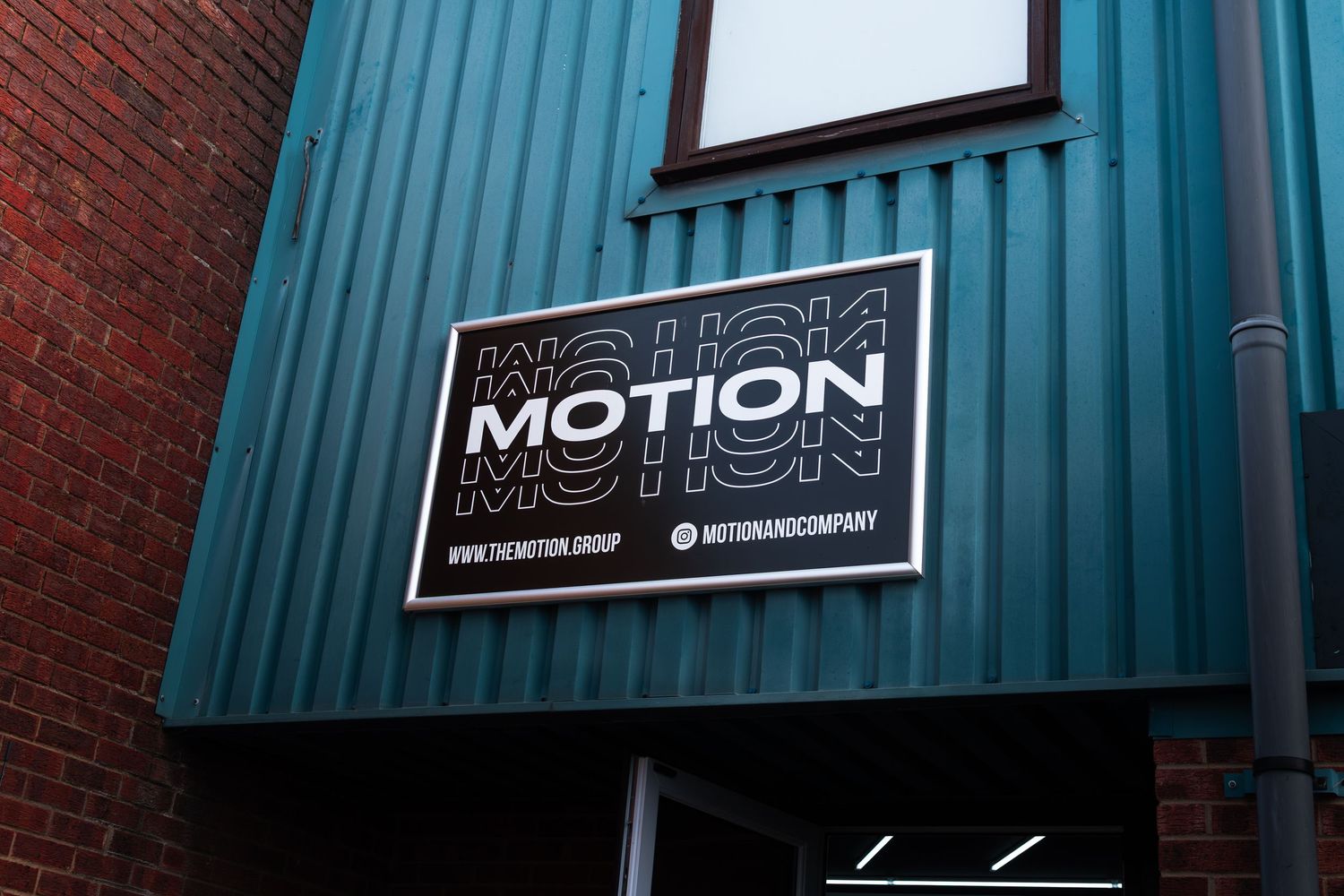 Motion Group company sign mounted on a teal corrugated metal building exterior wall.
