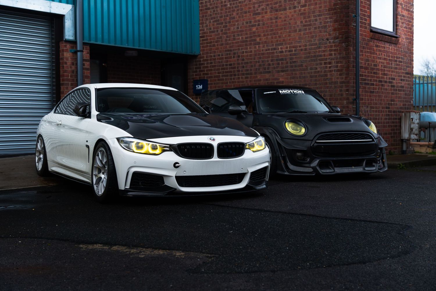 A white BMW 4 Series with yellow angel eyes parked next to a black Mini Cooper.