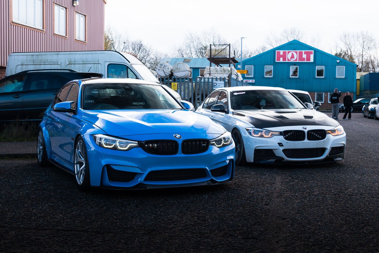 Two BMW M3 sedans, one blue and one white, parked side by side in a lot.