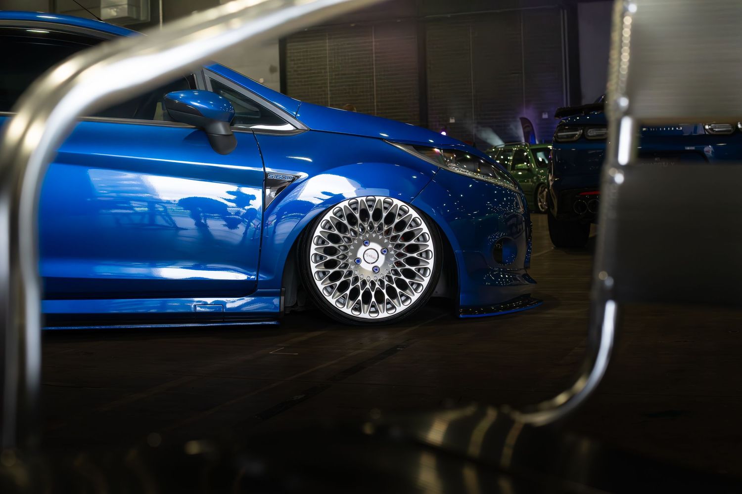 A lowered blue Ford Focus RS with polished multi-spoke alloy wheels on display at a car show.