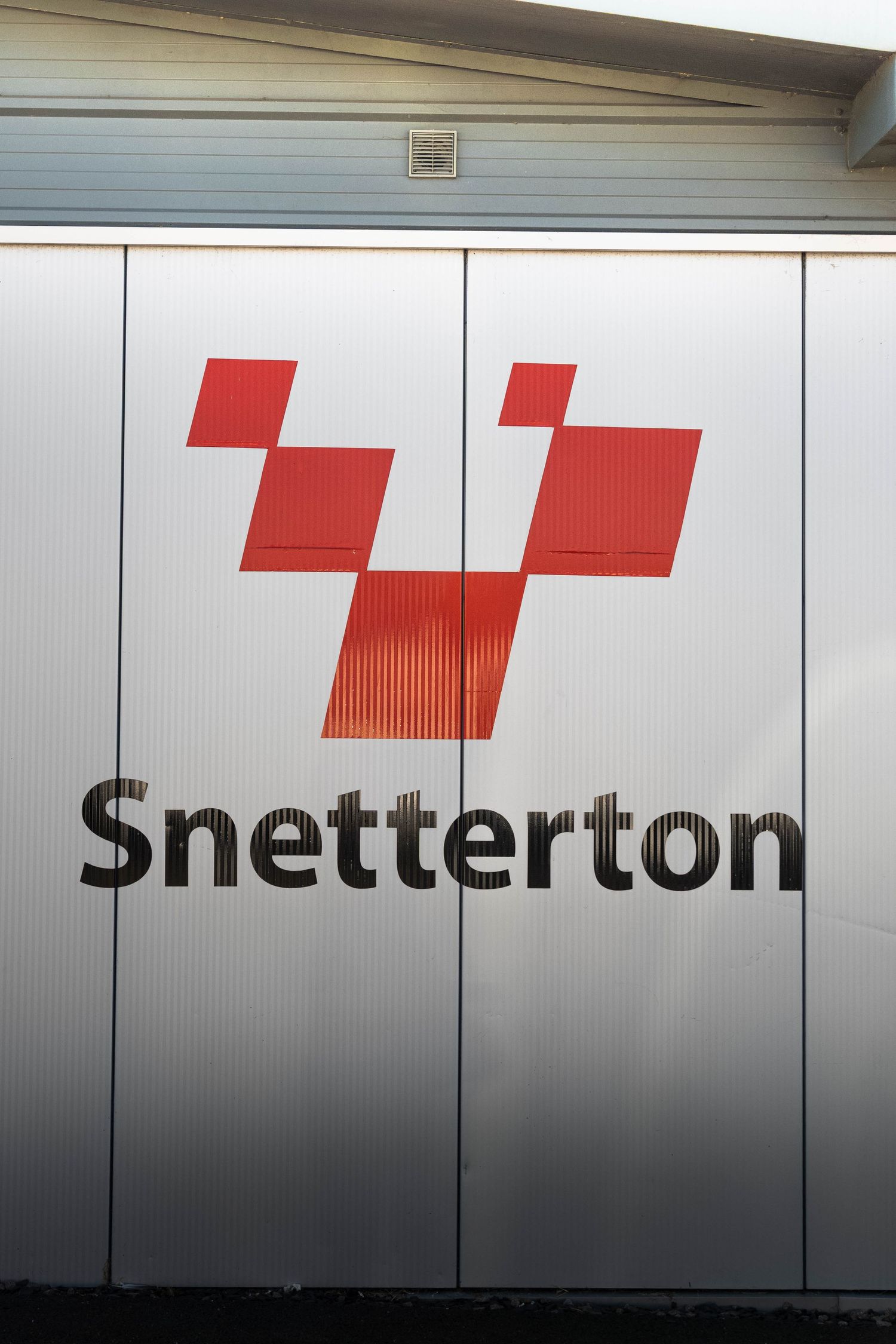 Snetterton motorsport circuit logo sign on silver corrugated metal building exterior wall.