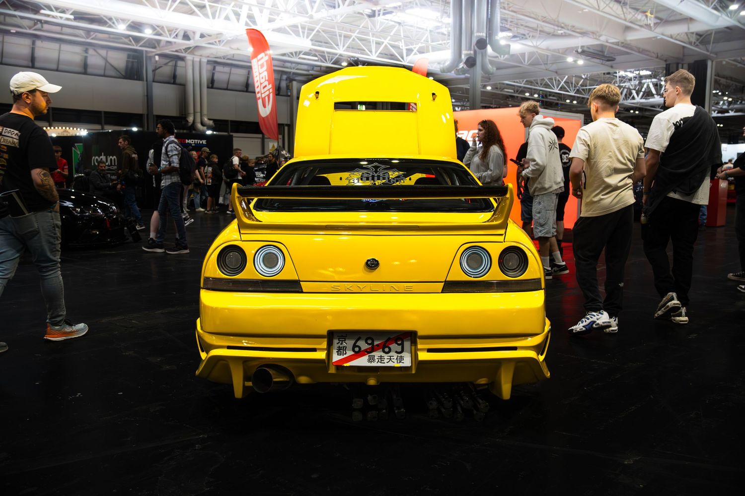 Yellow Nissan Skyline R33 GT-R rear view with quad exhausts at indoor motorsport expo.