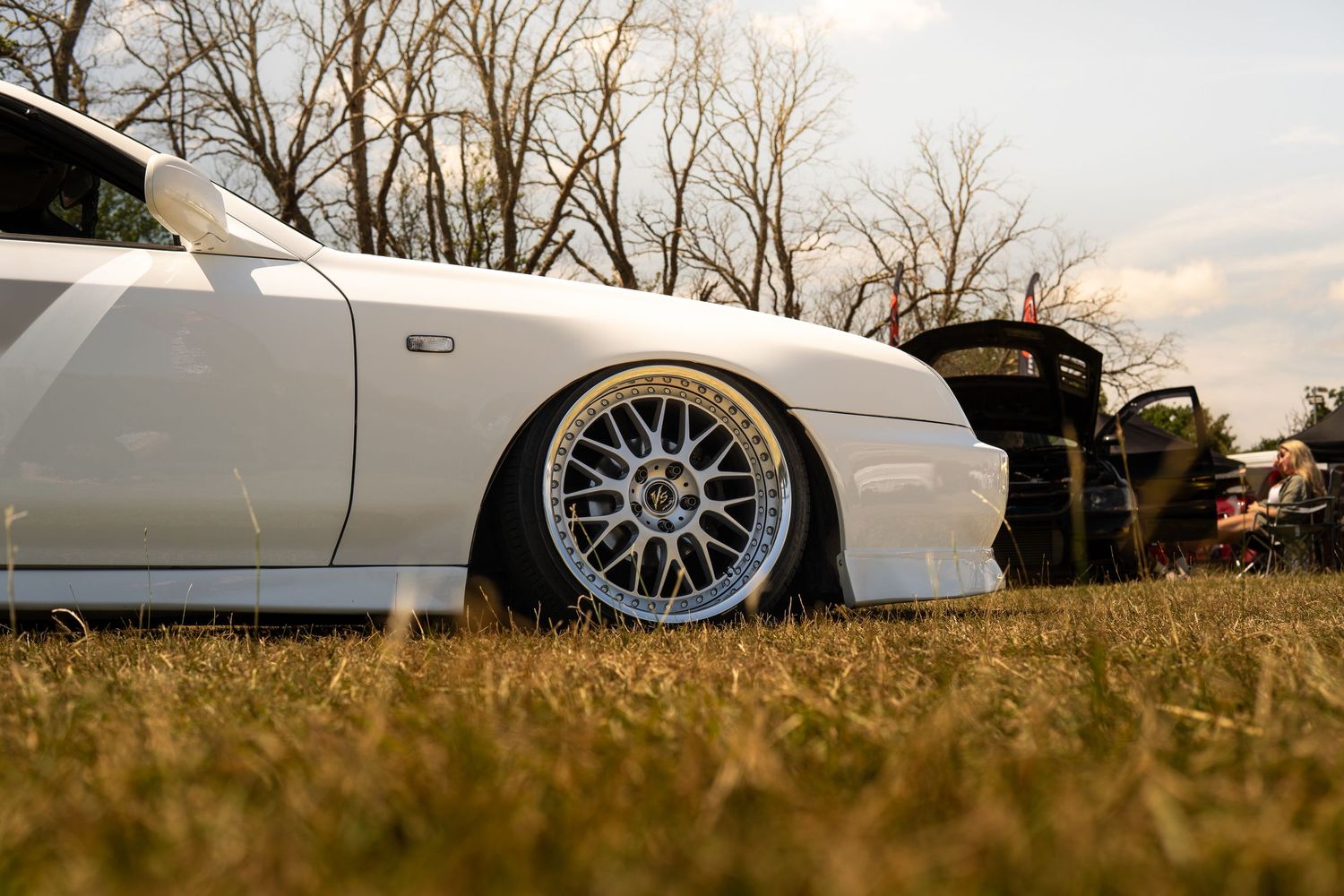 Low stance white modified car with BBS wheels on grass at a car show.