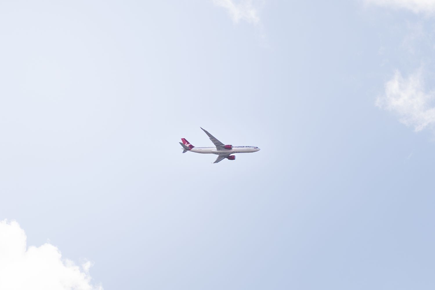 White and red commercial airplane flying through a partly cloudy blue sky.