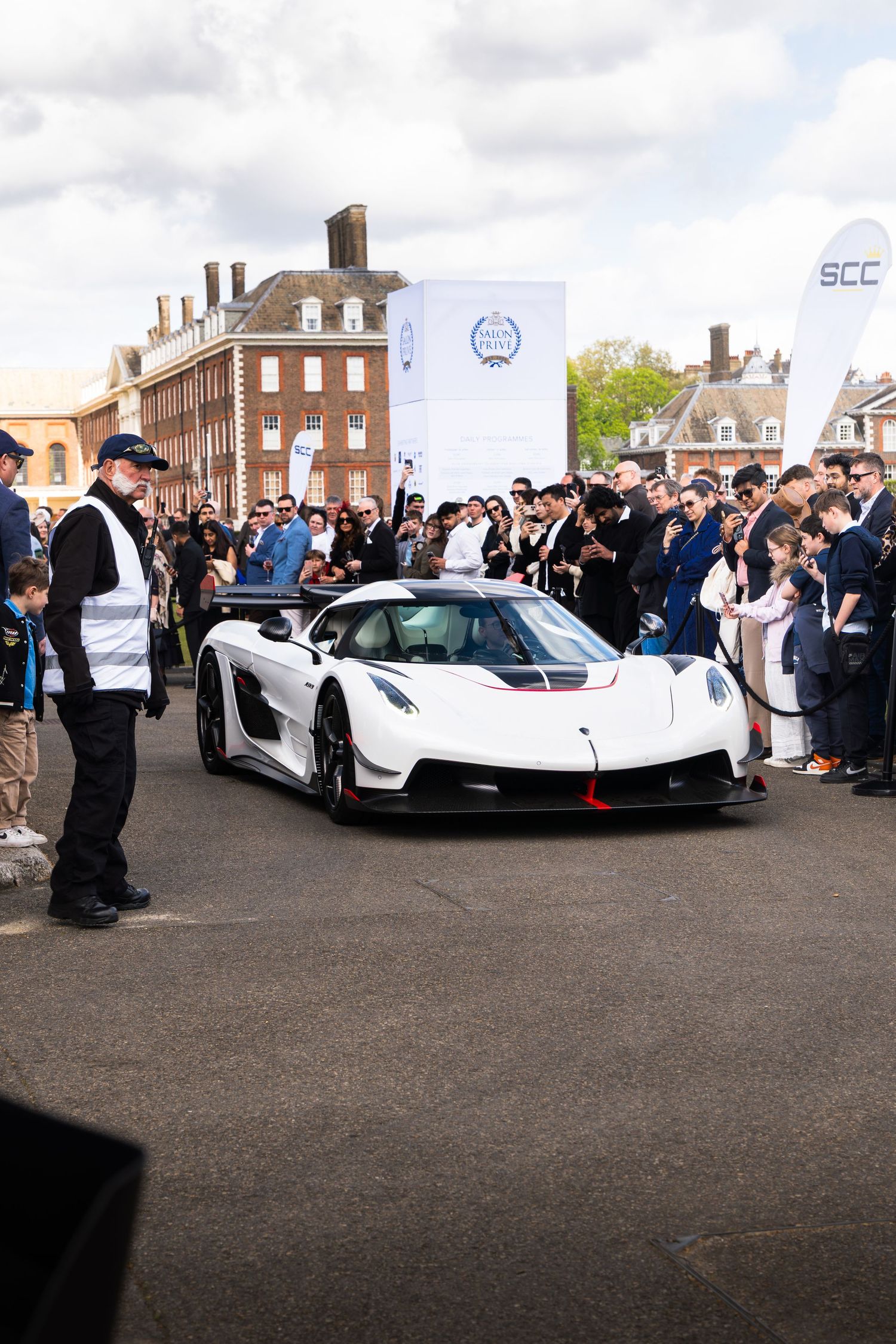 White Koenigsegg Jesko hypercar surrounded by a large crowd at an exclusive outdoor supercar event.