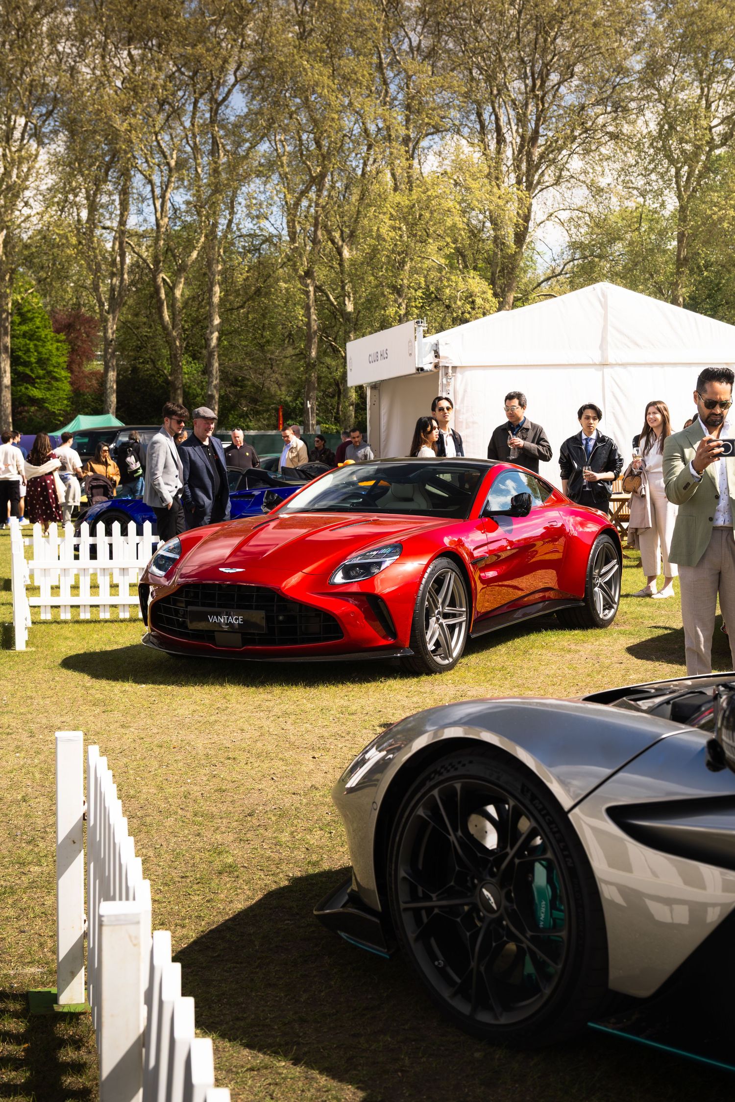 Red Aston Martin Vantage supercar on display surrounded by spectators at an outdoor automotive show.
