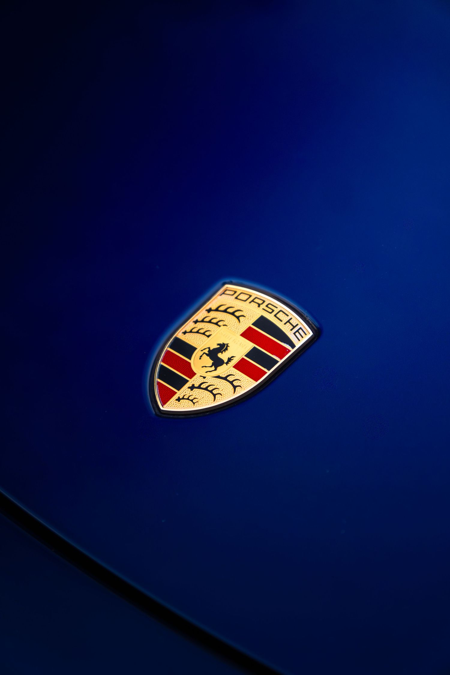 Close-up of Porsche crest badge on deep blue metallic hood of a Porsche sports car.
