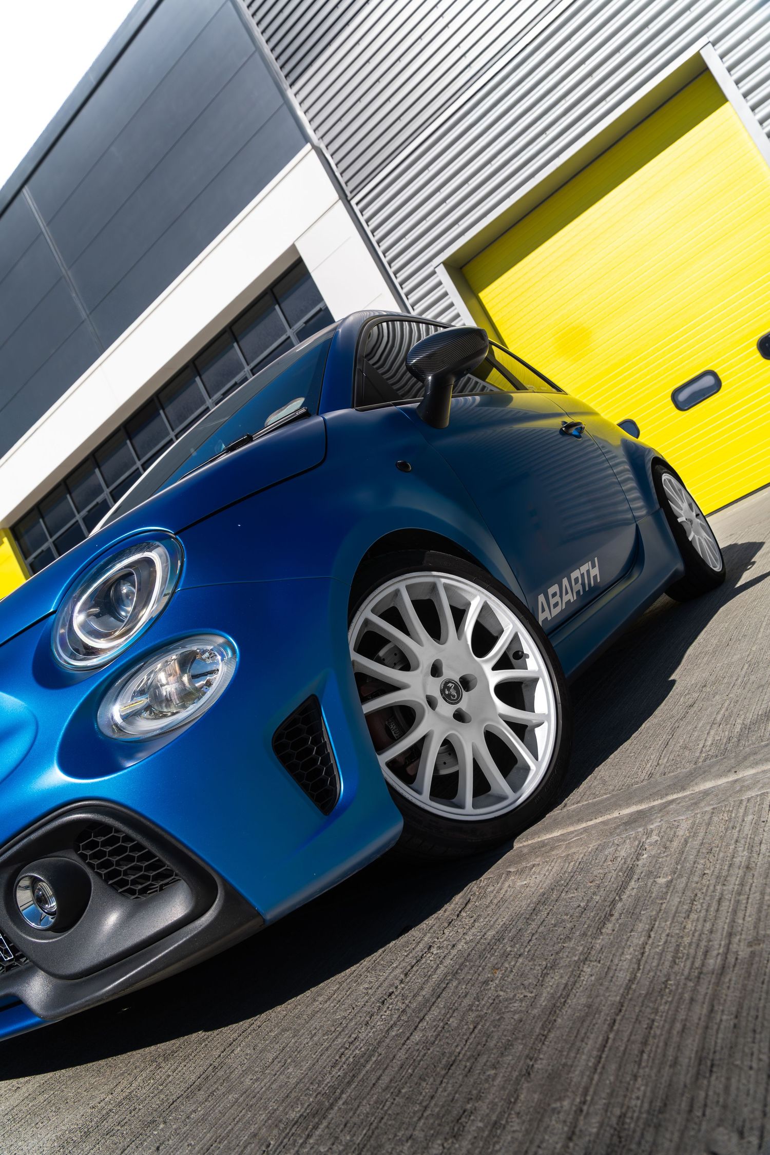 Close-up front corner view of a blue Abarth 500 showing alloy wheels and aggressive bumper.