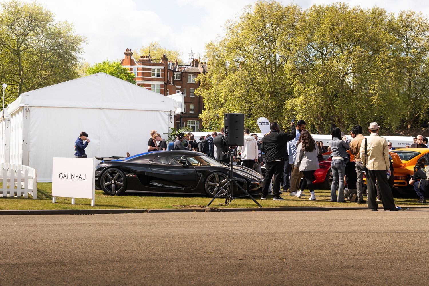 A sleek black Koenigsegg supercar on display at the Gatineau outdoor luxury automotive show with crowds.