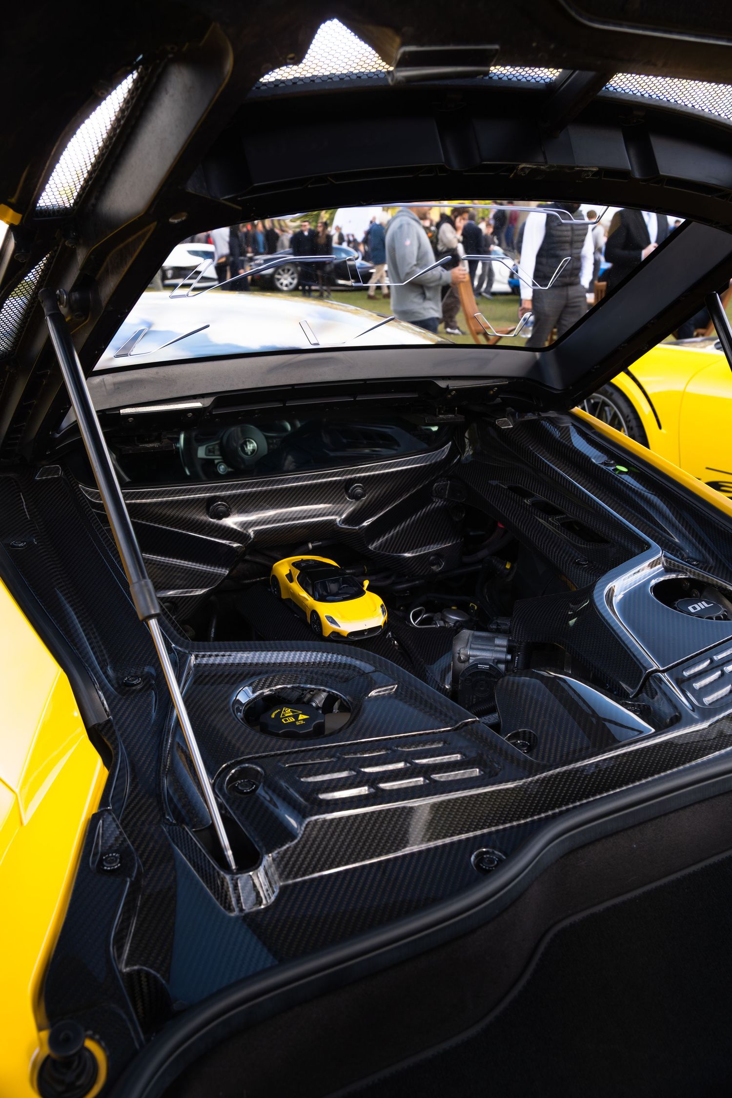 Carbon fiber engine bay of a yellow supercar with hood open at an auto show.