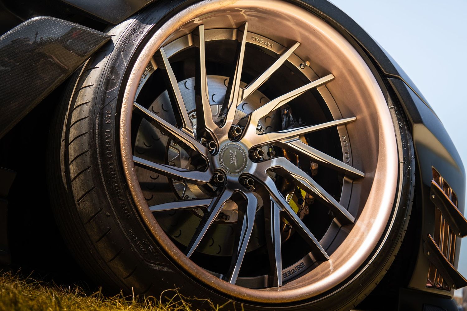 Luxury sports car with bronze multi-spoke alloy wheel and low-profile tire on grass.