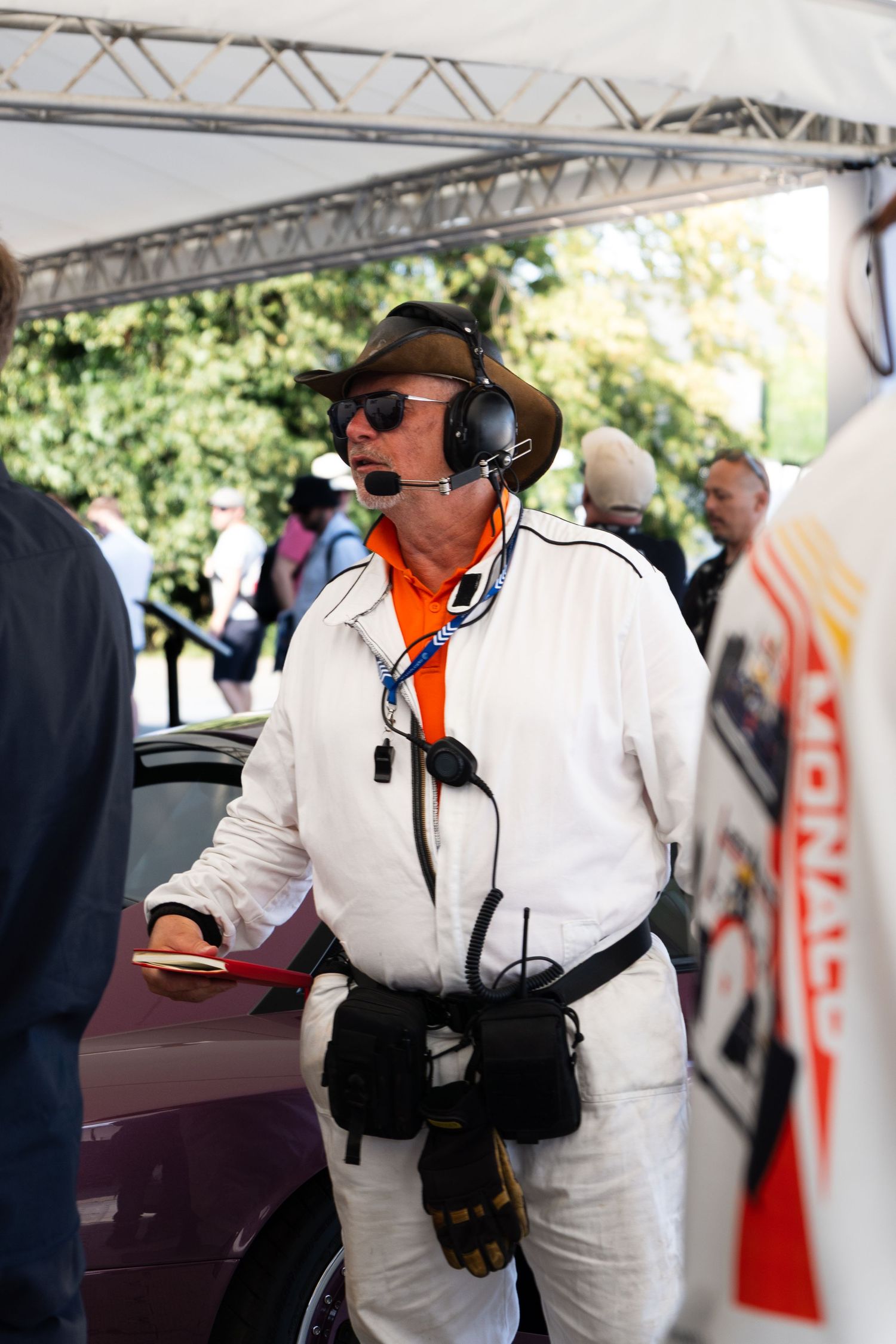 Race official in white jumpsuit wearing headset and hat stands under tent at Monaco racing event.