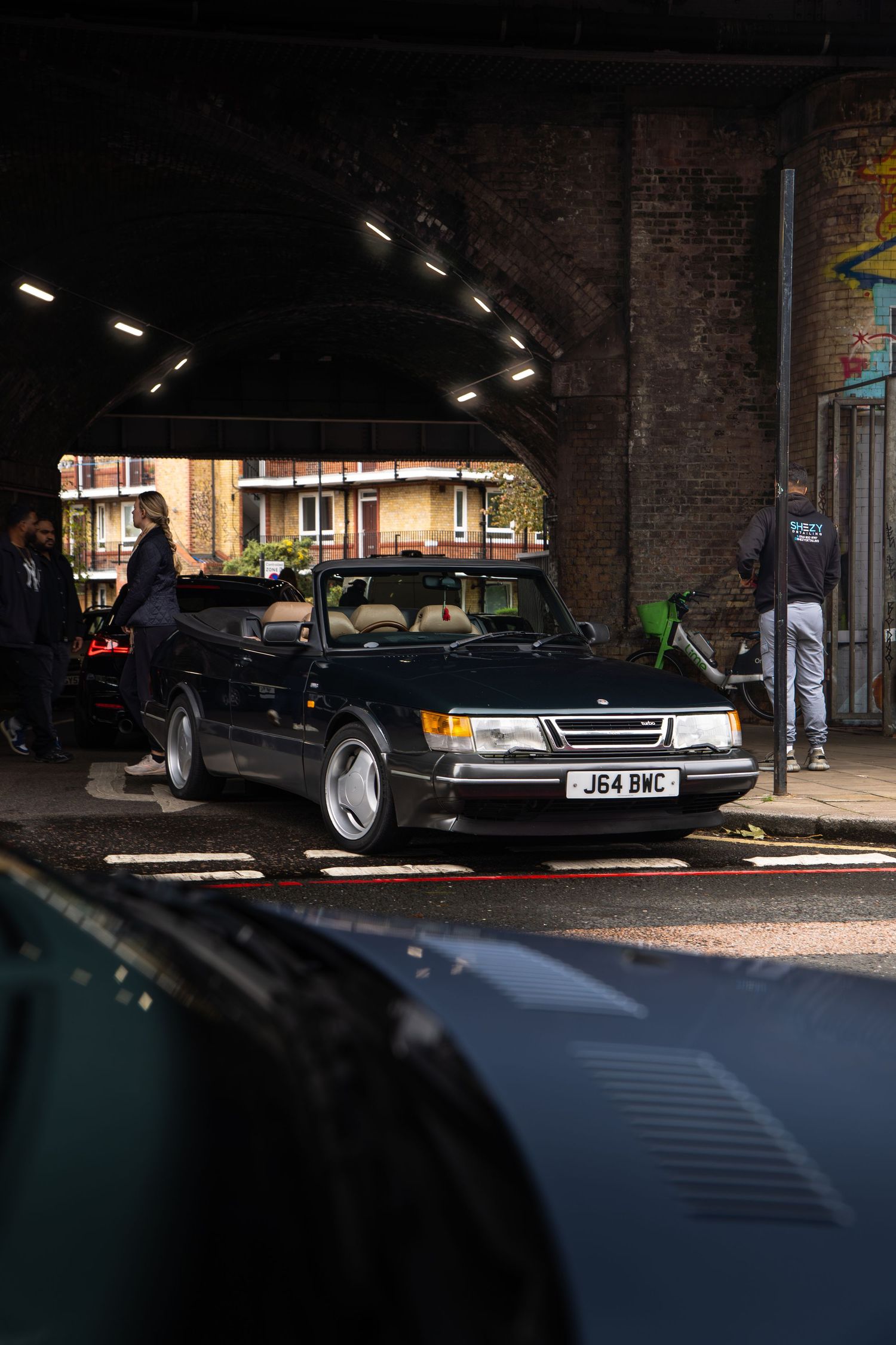 Classic black Saab 900 convertible parked under brick archway on urban street.