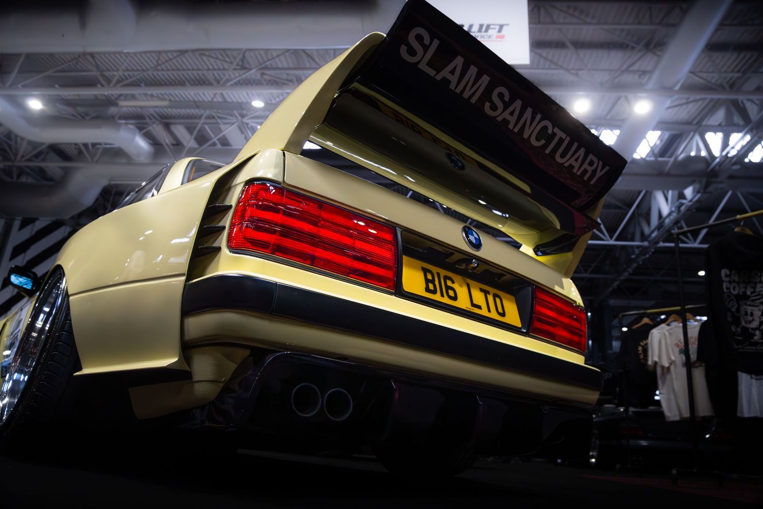 Rear view of pale yellow BMW E30 with Slam Sanctuary banner and BIG LTD number plate.