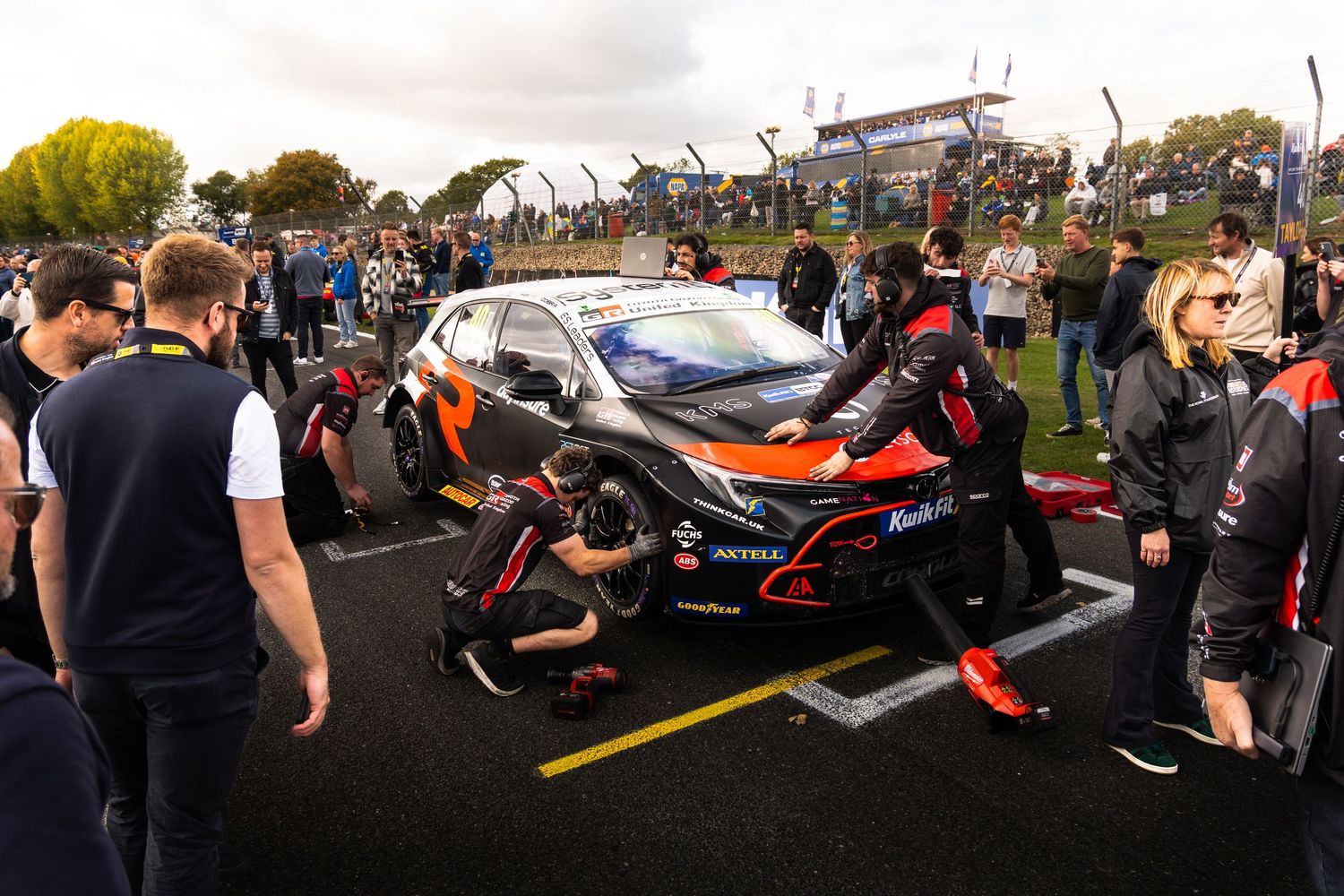 BTCC race car being serviced by mechanics on the starting grid surrounded by spectators.