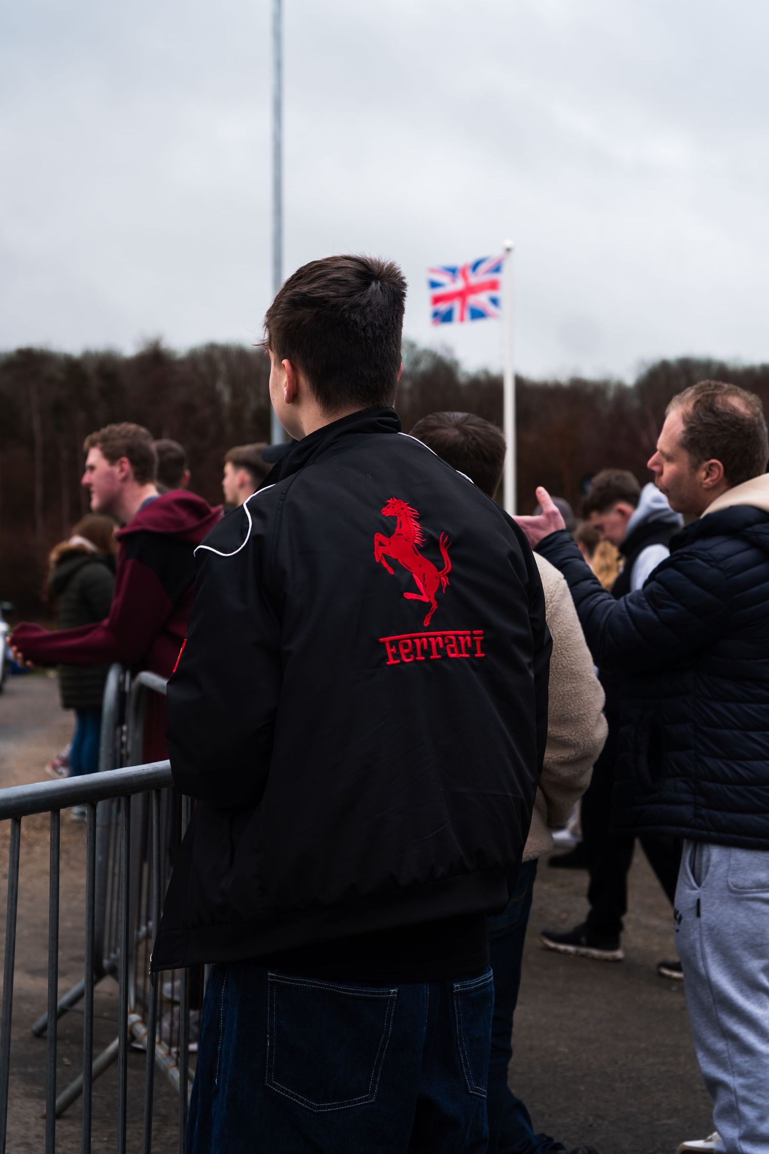 Person wearing Ferrari jacket at a UK car show with British flag in background.