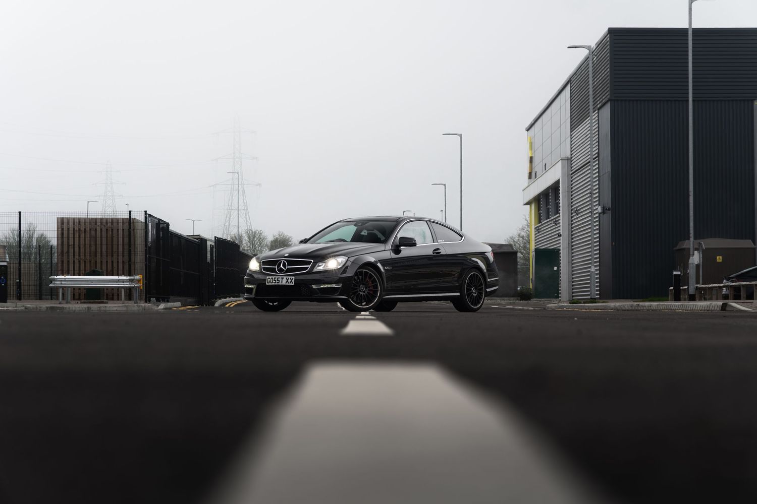 Black Mercedes-Benz C-Class AMG coupe parked on misty industrial estate road.