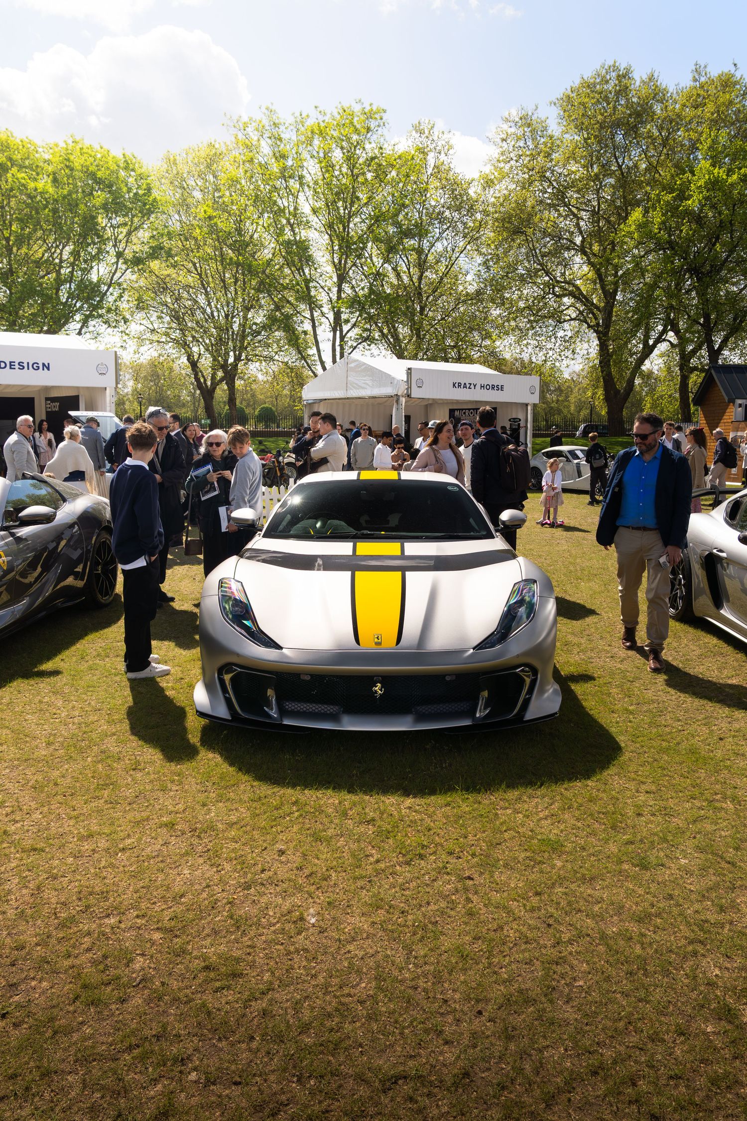 White Ferrari 812 Competizione with yellow stripes on display at an outdoor car show.