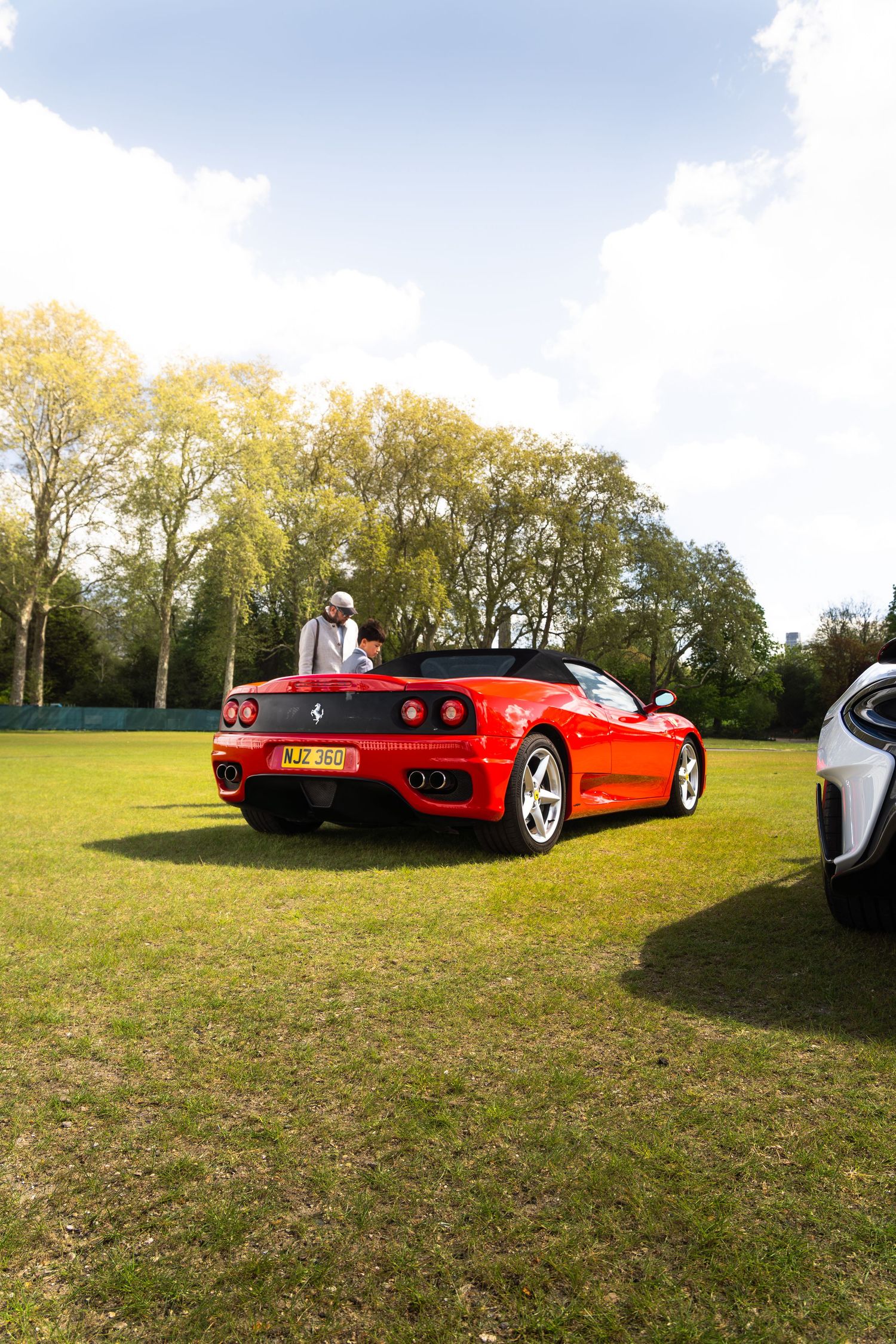 Red Ferrari 360 Spider convertible parked on grass at an outdoor car show event on a sunny day.
