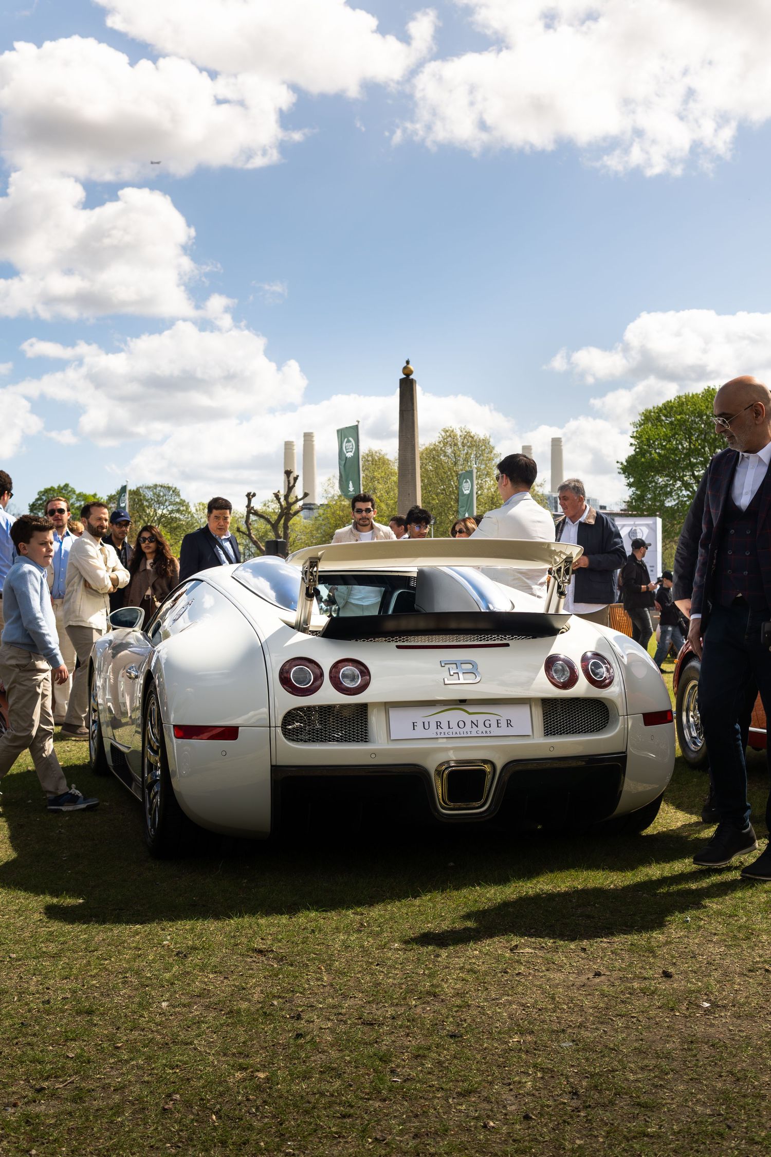 Rear view of a white Bugatti Veyron supercar surrounded by admirers at an outdoor luxury car show.