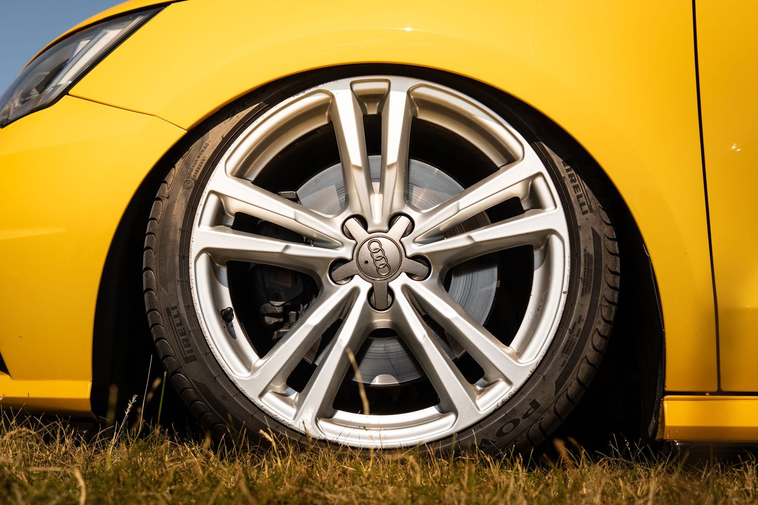 Close-up of silver Audi multi-spoke alloy wheel on lowered yellow car on grass.