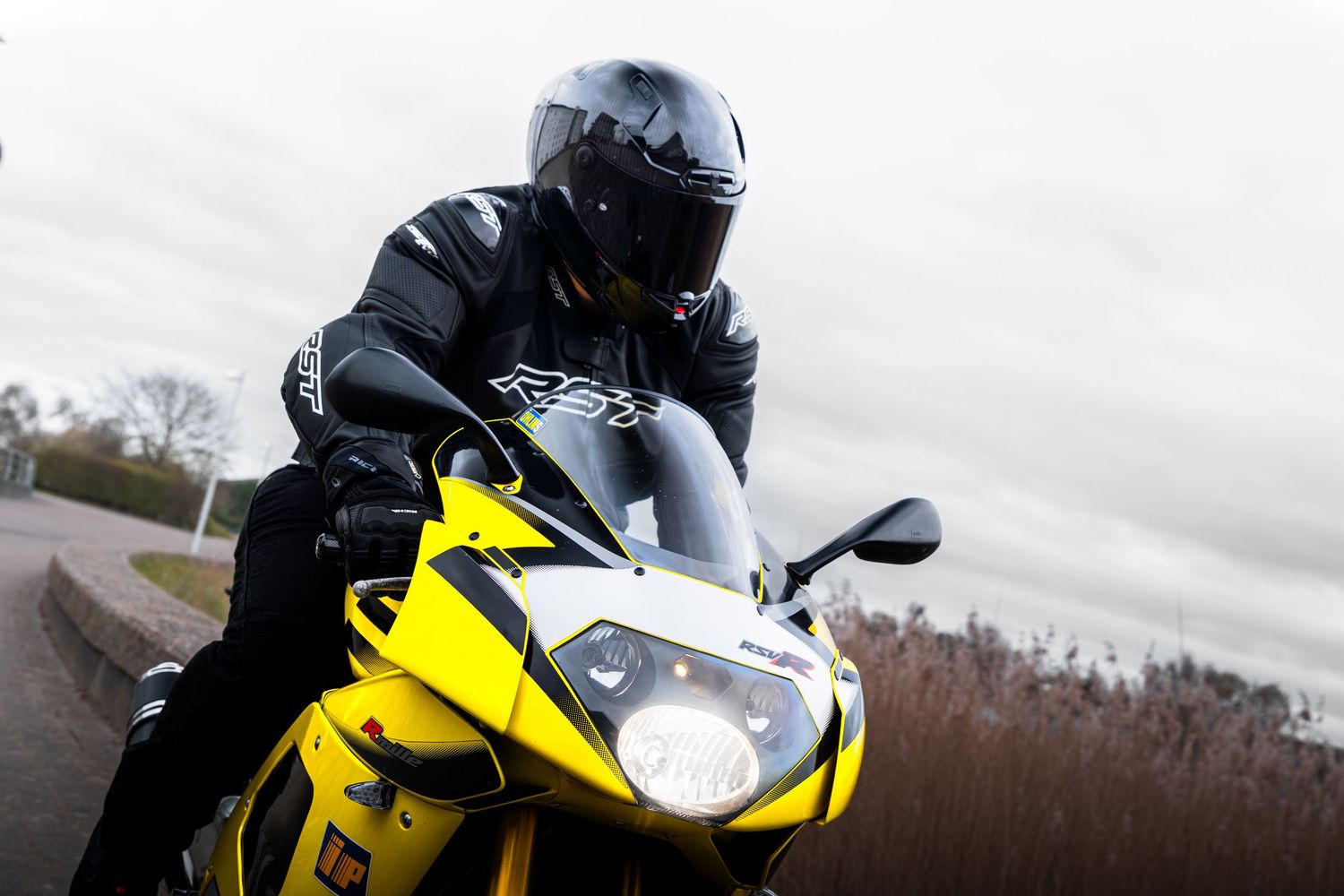Low-angle view of a rider in black RST gear leaning over a yellow Aprilia sports motorcycle.